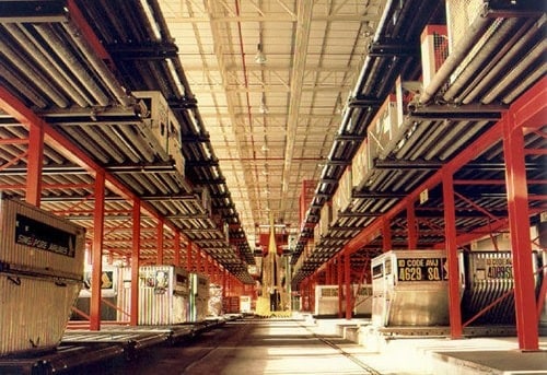 Expansive warehouse interior with rows of shelving, metal beams, and industrial equipment.