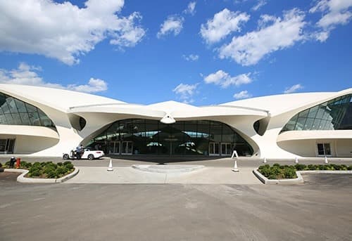 Sweeping modern airport terminal with curved roofs and glass walls under a blue sky with clouds.