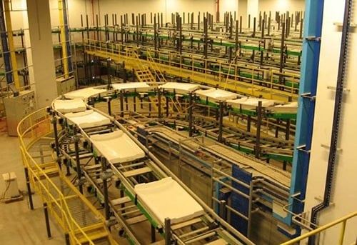 An industrial production facility with rows of machinery, conveyors, and storage shelves.