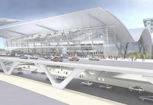 Modern airport terminal with dramatic architecture, busy with vehicles and pedestrians.