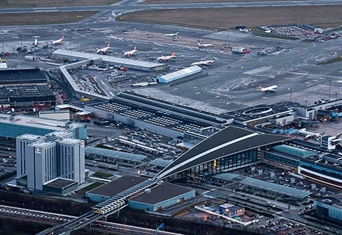Aerial view of a busy international airport terminal with multiple runways, planes, and buildings.