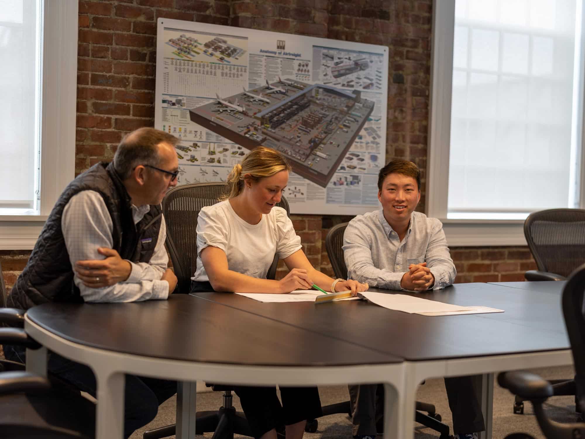 Three professionals reviewing documents in an office with a large wall map.