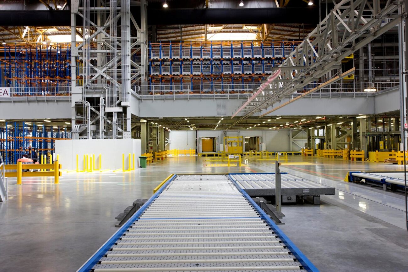 Vast warehouse interior with rows of shelves, conveyor belts, and machinery - a busy cargo distribution facility.