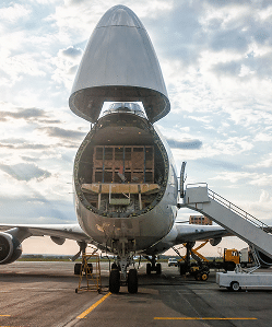 Large cargo aircraft with open rear cargo door at airport terminal.