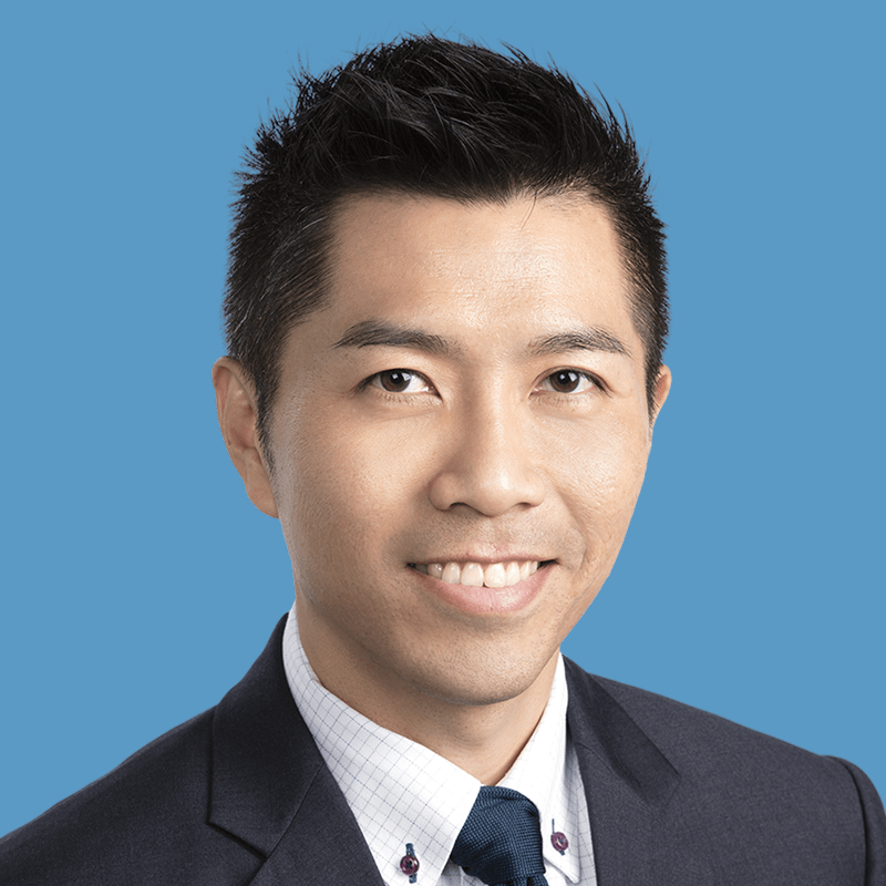 Portrait of a smiling man in a dark suit against a blue background.