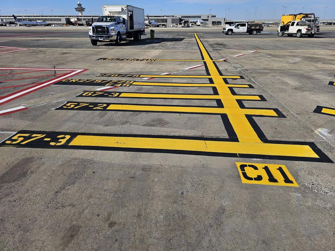 Striped airport pavement markings with vehicle parking spots and aircraft taxis on a sunny day.
